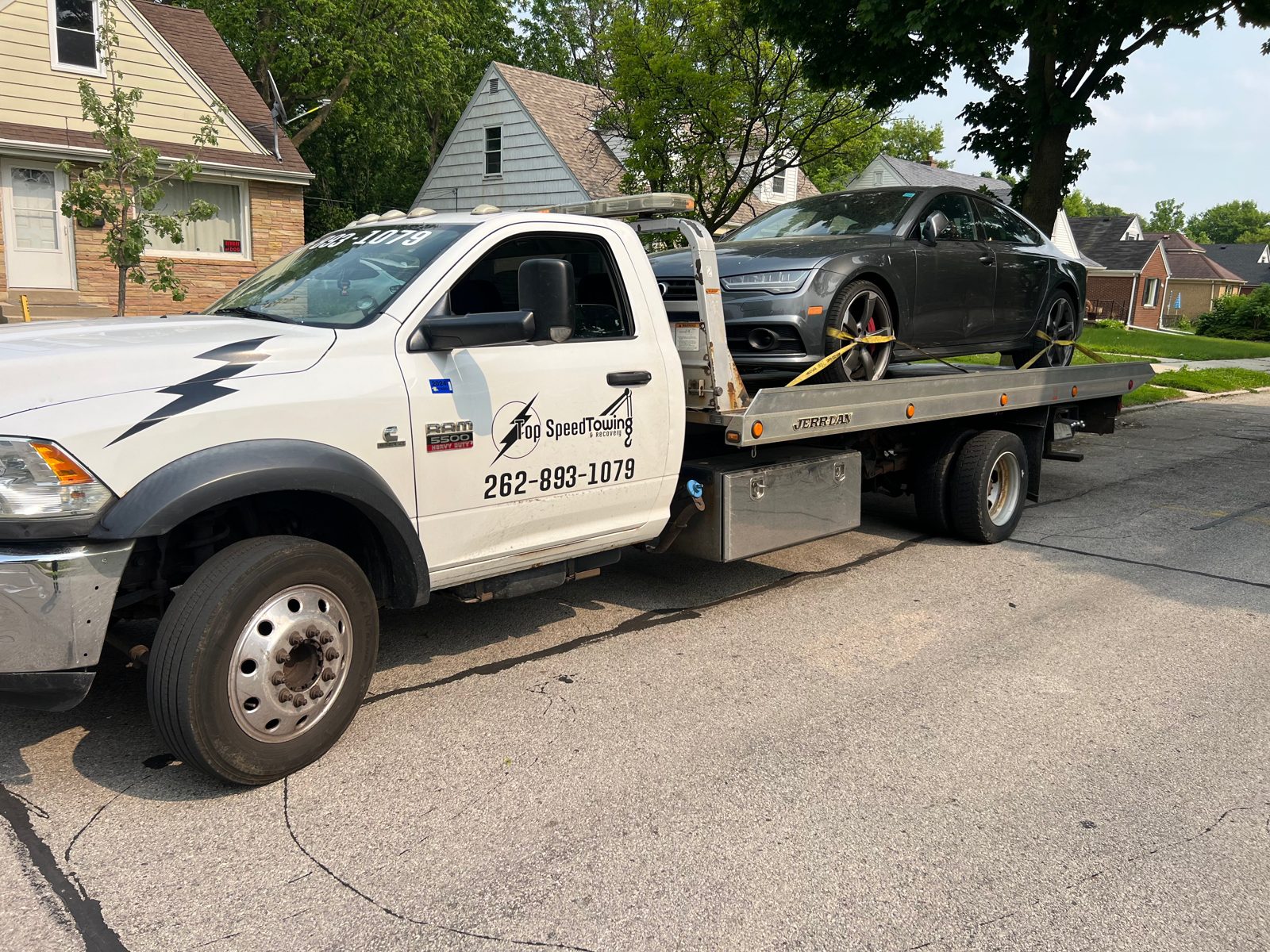 Flatbed towing a luxury car in a Milwaukee neighborhood